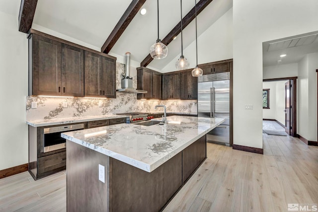 kitchen with a center island with sink, wall oven, dark brown cabinetry, wall chimney range hood, and built in refrigerator