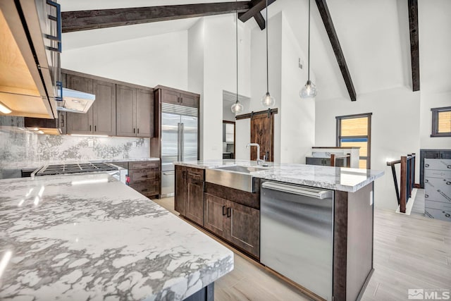 kitchen featuring light stone counters, pendant lighting, stainless steel appliances, a barn door, and an island with sink