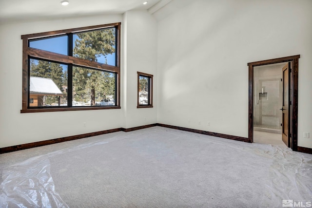 empty room with high vaulted ceiling, light colored carpet, and baseboards