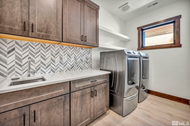 laundry area with washing machine and dryer, a sink, visible vents, light wood-type flooring, and cabinet space