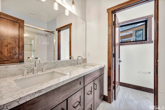 bathroom featuring a tile shower, double vanity, a sink, and baseboards