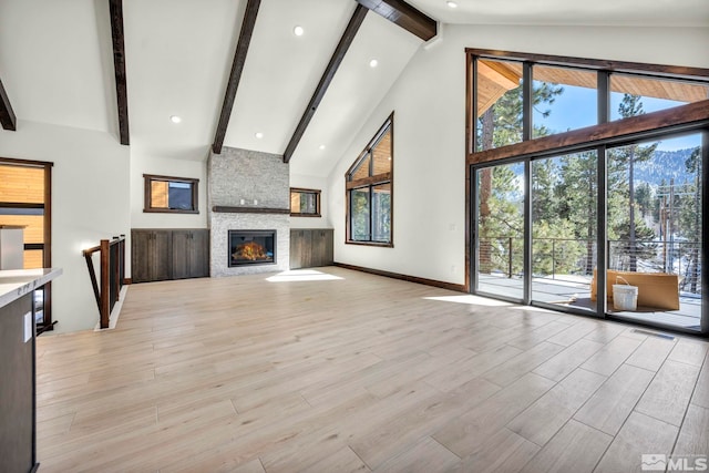 unfurnished living room featuring high vaulted ceiling, a stone fireplace, beamed ceiling, and light wood-style floors