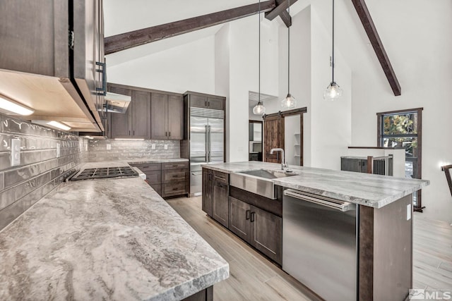 kitchen with a barn door, dark brown cabinetry, stainless steel appliances, hanging light fixtures, and a center island with sink