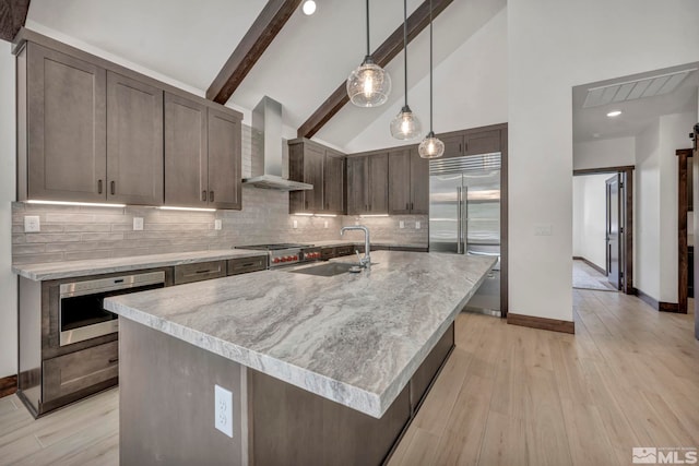 kitchen with decorative light fixtures, a center island with sink, light countertops, stainless steel built in fridge, and wall chimney range hood