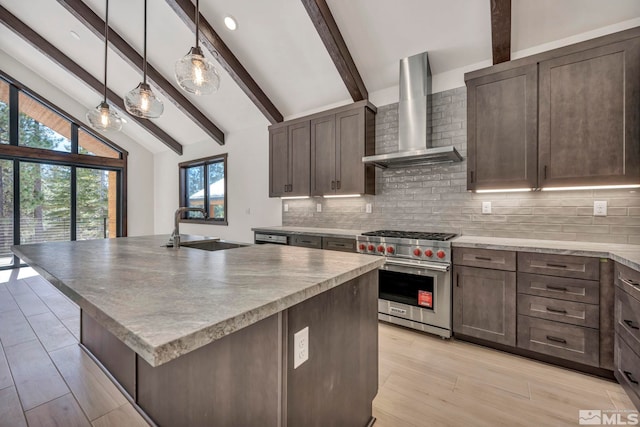 kitchen featuring hanging light fixtures, a sink, wall chimney range hood, an island with sink, and luxury stove