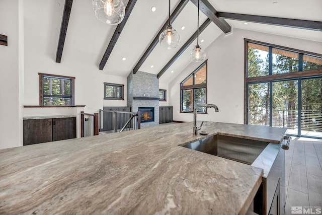 kitchen featuring a fireplace, hanging light fixtures, a healthy amount of sunlight, a sink, and high vaulted ceiling