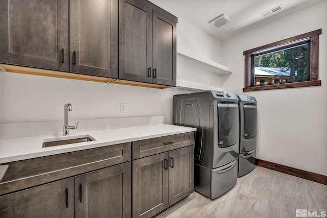 clothes washing area featuring washing machine and dryer, a sink, visible vents, baseboards, and cabinet space