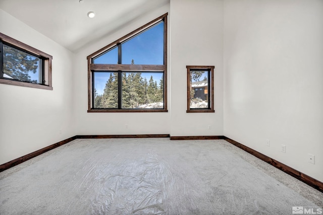 empty room featuring carpet flooring, vaulted ceiling, and baseboards