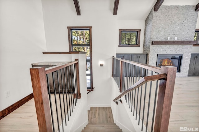 staircase featuring beam ceiling, a fireplace, baseboards, and wood finished floors