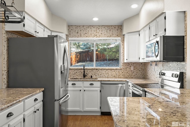 kitchen with appliances with stainless steel finishes, white cabinetry, a sink, and decorative backsplash