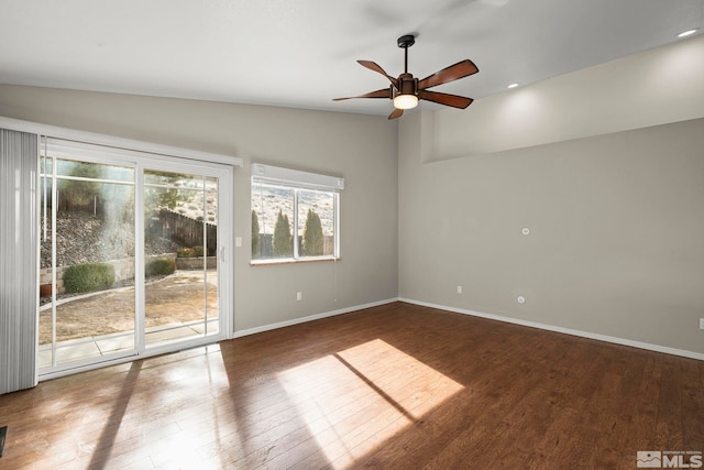 spare room featuring vaulted ceiling, dark wood-type flooring, a ceiling fan, and baseboards