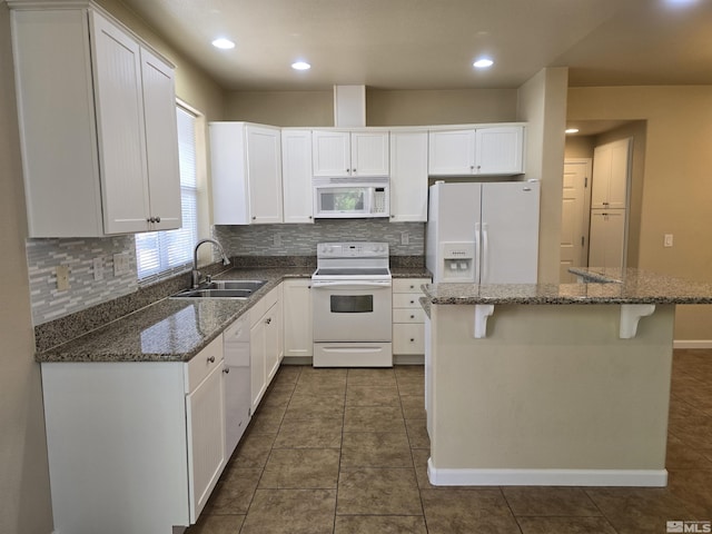 kitchen with white appliances, dark stone counters, white cabinets, a center island, and a sink