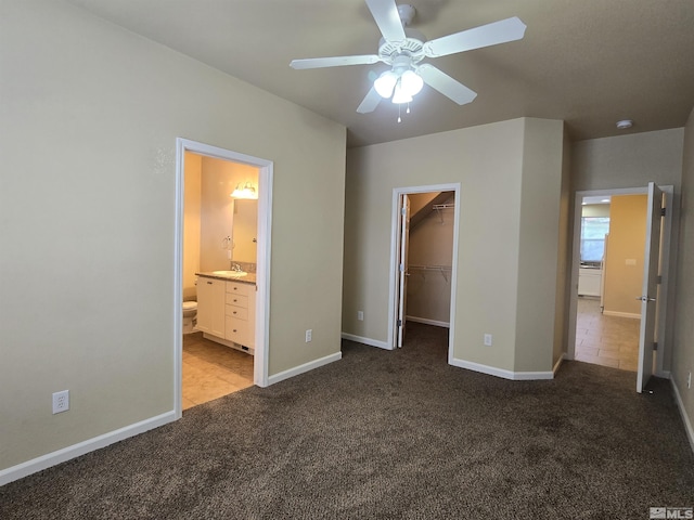 unfurnished bedroom with baseboards, a sink, a walk in closet, and light colored carpet