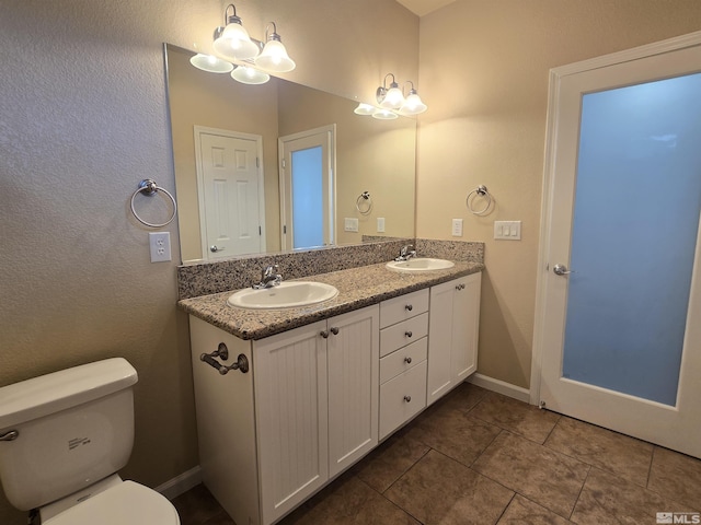 bathroom with toilet, double vanity, baseboards, and a sink