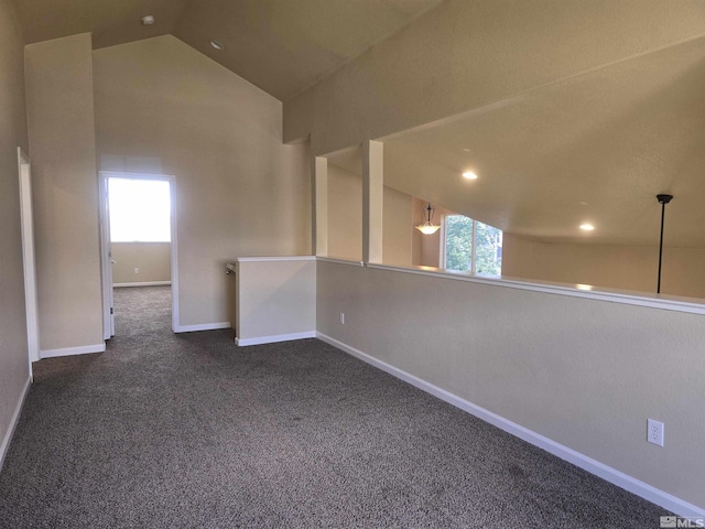 spare room featuring lofted ceiling, dark carpet, and baseboards