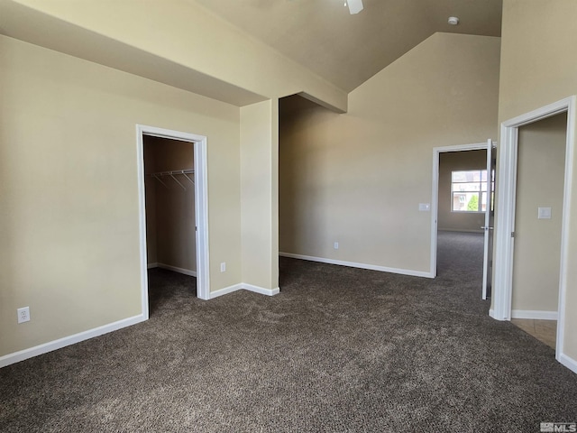 unfurnished bedroom with vaulted ceiling, dark carpet, a walk in closet, and baseboards