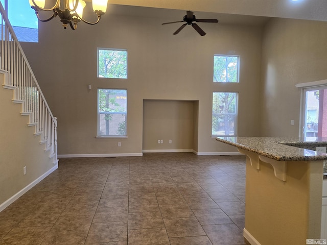 unfurnished living room featuring baseboards, stairway, tile patterned floors, a high ceiling, and ceiling fan with notable chandelier