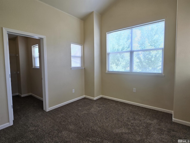 empty room with dark colored carpet, plenty of natural light, and baseboards