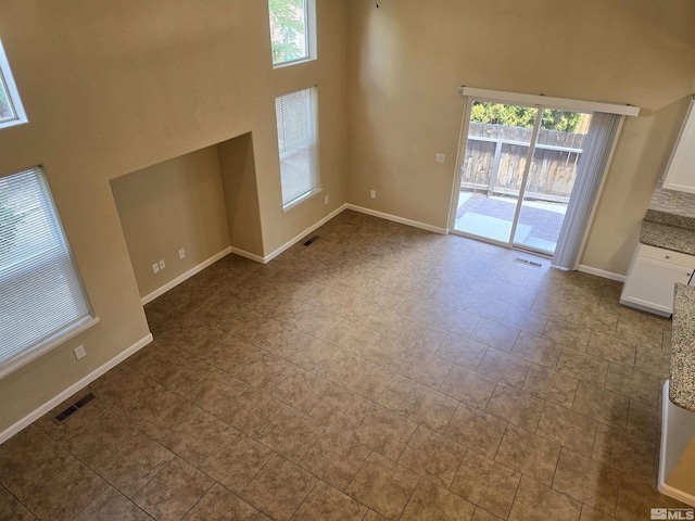 unfurnished living room featuring a high ceiling, visible vents, and baseboards