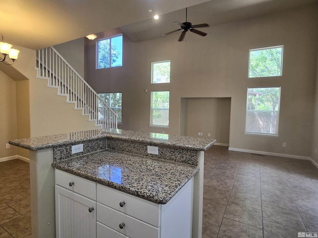 kitchen with a towering ceiling, open floor plan, white cabinets, dark stone counters, and dark tile patterned floors