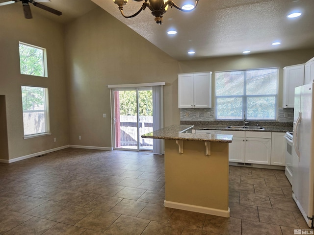 kitchen with a breakfast bar, white cabinets, a kitchen island, a sink, and dark stone countertops