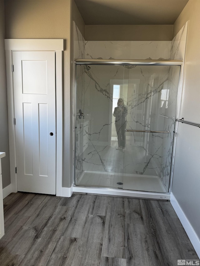 full bath featuring a marble finish shower, baseboards, and wood finished floors