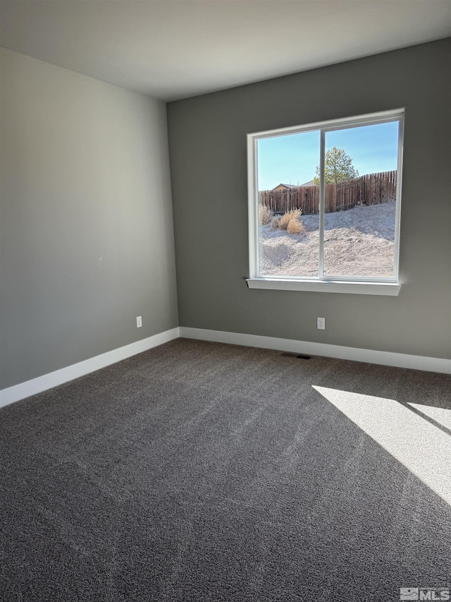 spare room featuring visible vents, baseboards, and dark carpet