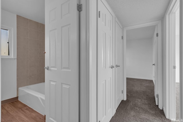 hallway featuring carpet, a textured ceiling, baseboards, and wood finished floors