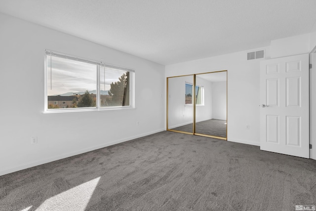 unfurnished bedroom featuring baseboards, visible vents, dark colored carpet, and a closet