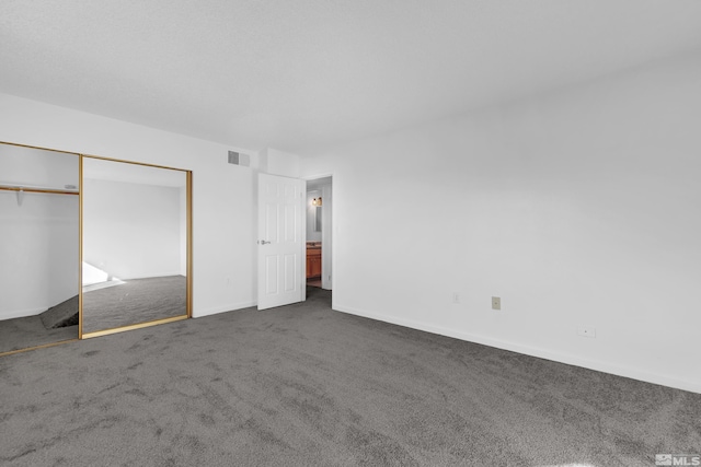 unfurnished bedroom featuring baseboards, visible vents, dark colored carpet, and a closet