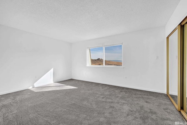 empty room featuring a textured ceiling, dark carpet, and baseboards