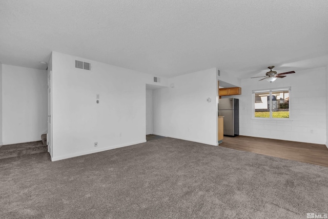 unfurnished living room featuring a textured ceiling, dark colored carpet, and visible vents