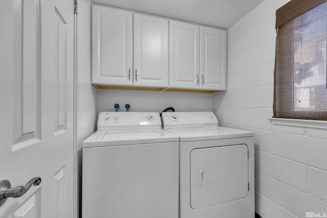 washroom featuring concrete block wall, cabinet space, and separate washer and dryer