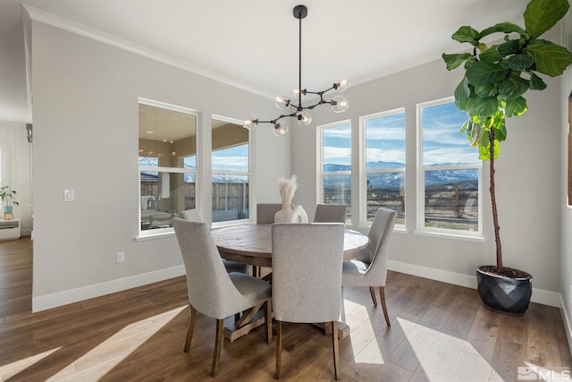 dining space with dark wood-style flooring, a notable chandelier, crown molding, a mountain view, and baseboards