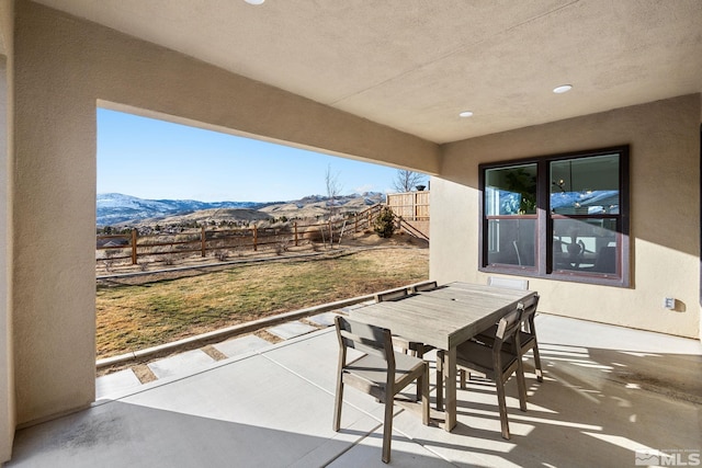 view of patio featuring outdoor dining space, a mountain view, and fence