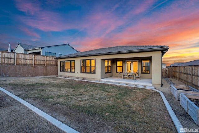 rear view of house with a yard, a patio, stucco siding, a fenced backyard, and a garden