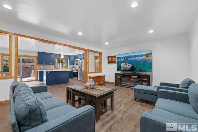 living area featuring baseboards, light wood-type flooring, a glass covered fireplace, and recessed lighting