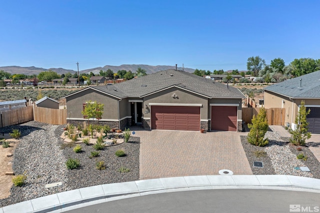 single story home with stone siding, a mountain view, an attached garage, and fence