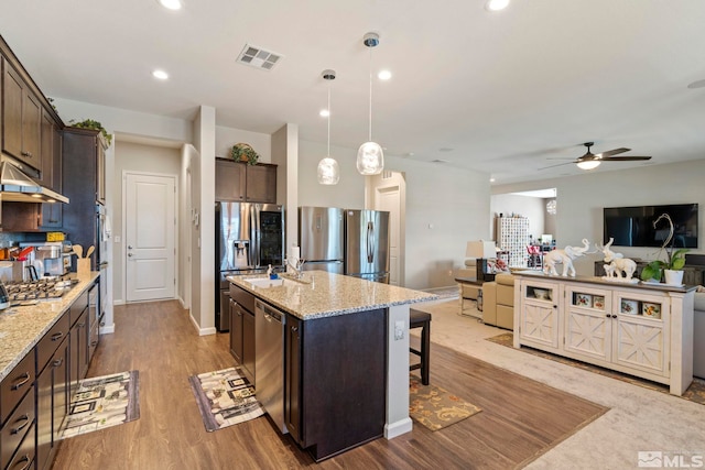 kitchen with appliances with stainless steel finishes, open floor plan, hanging light fixtures, a kitchen island with sink, and dark brown cabinets