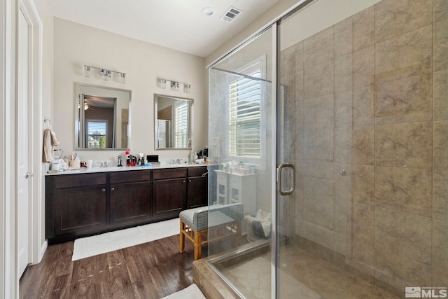 full bathroom with double vanity, visible vents, a stall shower, a sink, and wood finished floors