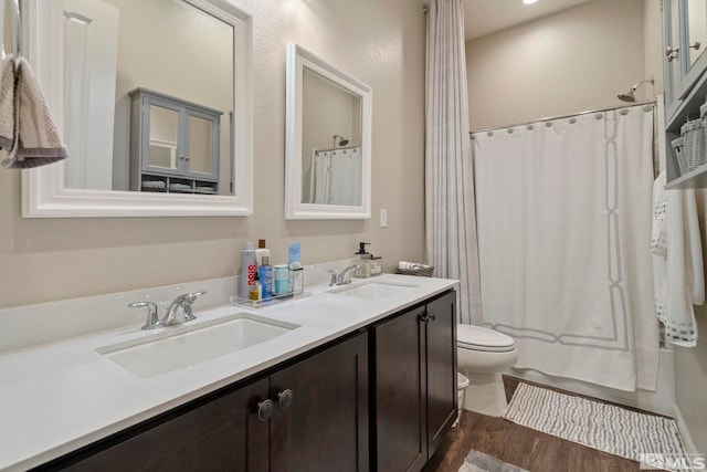 full bath with double vanity, wood finished floors, a sink, and toilet