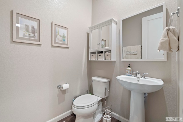 half bathroom with a sink, toilet, and baseboards