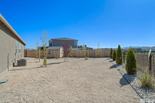 view of yard with an outbuilding, central AC unit, a fenced backyard, a mountain view, and a storage unit