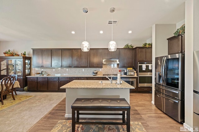 kitchen with decorative light fixtures, visible vents, appliances with stainless steel finishes, an island with sink, and under cabinet range hood