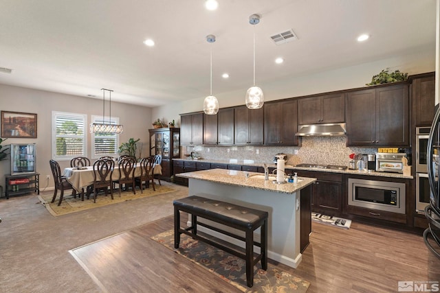 kitchen with decorative light fixtures, a center island with sink, stainless steel appliances, visible vents, and under cabinet range hood