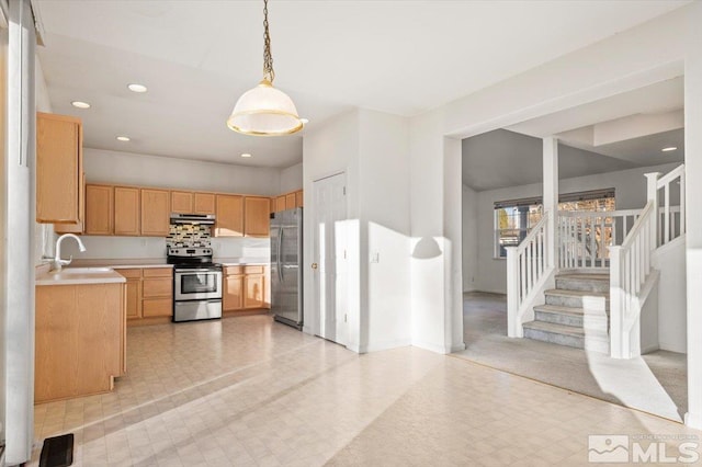 kitchen with under cabinet range hood, a sink, light countertops, appliances with stainless steel finishes, and pendant lighting