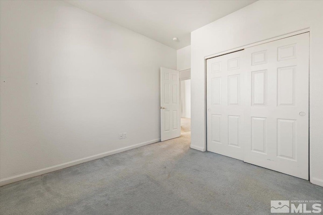 unfurnished bedroom featuring light carpet, baseboards, and a closet