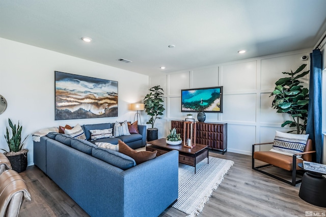 living room with recessed lighting, visible vents, a decorative wall, and wood finished floors