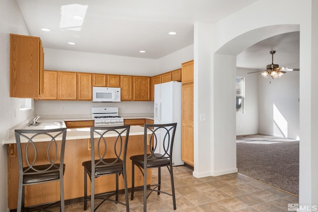 kitchen featuring light countertops, brown cabinetry, a sink, white appliances, and a peninsula