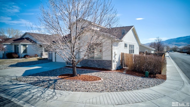 view of side of home featuring a mountain view, a garage, fence, concrete driveway, and stone siding